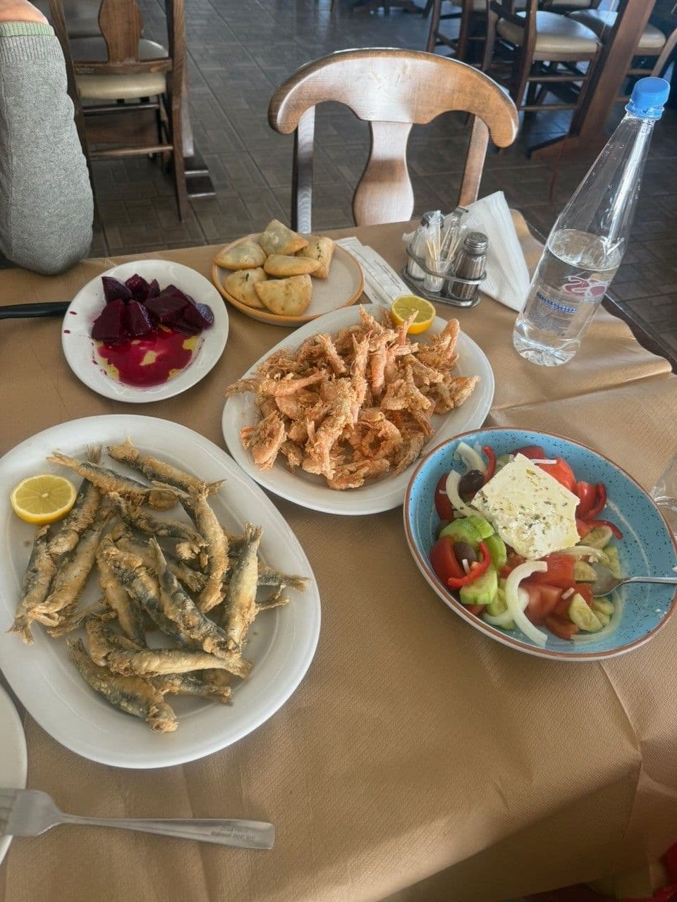 A taverna table with fried small fish, fried shrimp, beetroot, cheese pies and a Greek salad